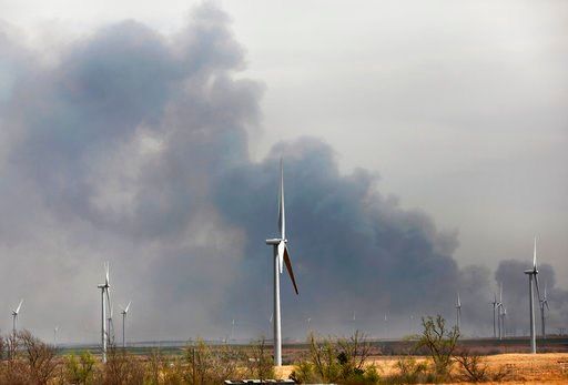 (Jim Beckel/The Oklahoman via AP). In this Tuesday, April 17, 2018, wind turbines dot the horizon of eastern Dewey County as heavy smoke from wildfires drift above a field west of Seiling, Okla.,