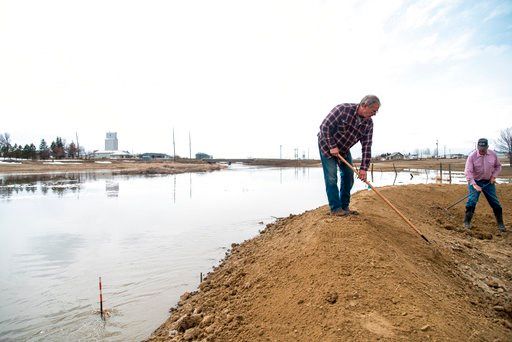 (Ryan Welch/Havre Daily News via AP). Lanay Kapperud, left, and Donald Miller use hoes Monday, April 16, 2018 to move dirt on a flood barrier that the town of Gildford constructed Sunday to protect their sewage systems and pump as rising water levels h...