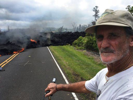 (AP Photo/Marco Garcia). Resident Sam Knox, 65, rides his bicycle to the edge of the road as lava burns across the road in the Leilani Estates in Pahoa, Hawaii, Saturday, May 5, 2018. Hundreds of anxious residents on the Big Island of Hawaii hunkered d...
