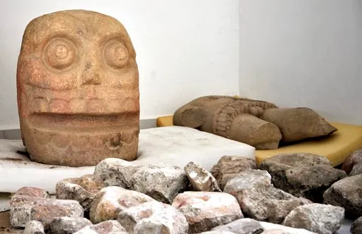 (Meliton Tapia Davila/INAH via AP). In this 2018 photo provided by Mexico's National Institute of Anthropology and History, INAH, a skull-like stone carving and a stone trunk depicting the Flayed Lord, a pre-Hispanic fertility god depicted as a skinned...