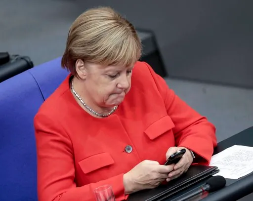 (Kay Nietfeld/dpa via AP). In this Sept.12, 2018 photo German Chancellor Angela Merkel (CDU) is looking at her mobile phone during the general debate in the German Bundestag.